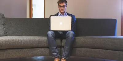 "Mann vor Laptop auf der Caoch"